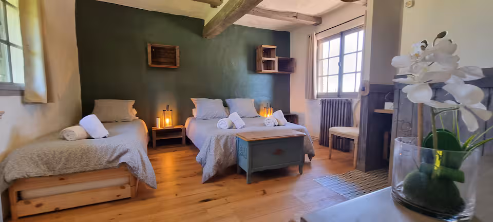 Chambre 2 avec mur vert sombre, lit double et lit simple d'appoint, coffre en bois patiné au pied du lit.