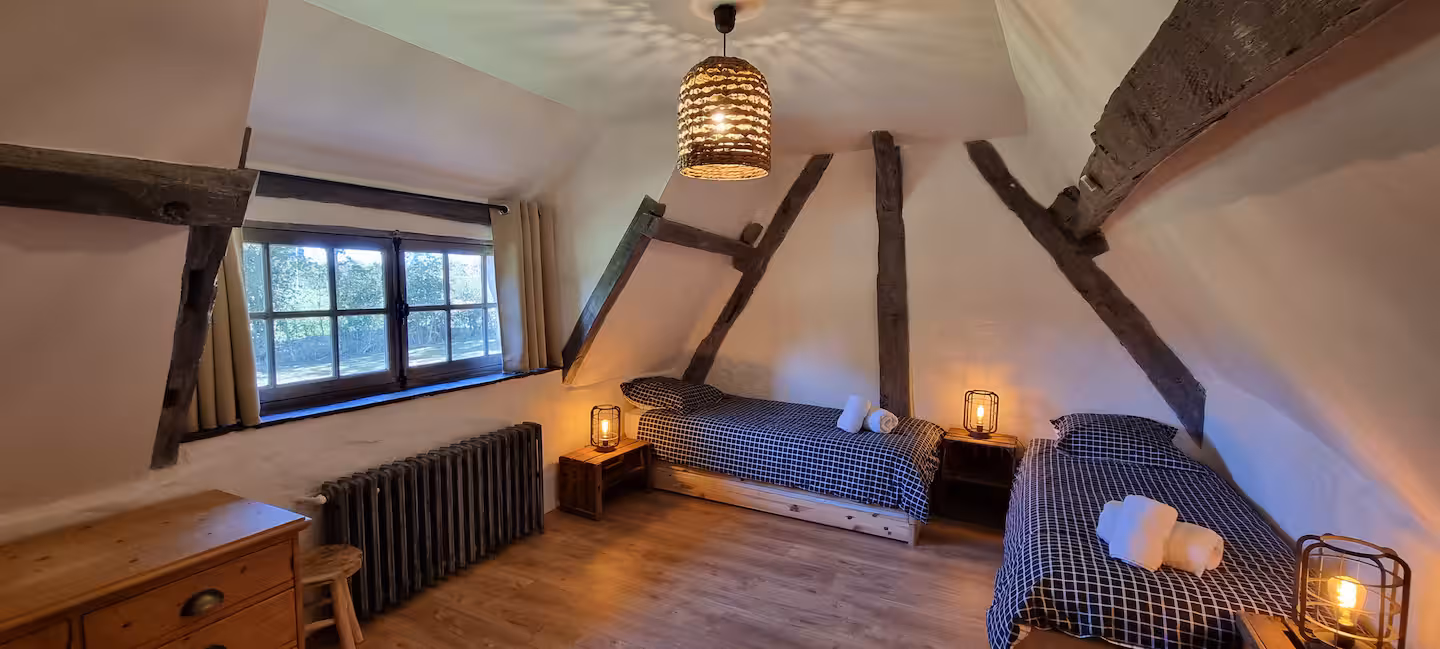 Chambre 3 sous combles avec lits simples séparés, charpente apparente en chêne et radiateur en fonte.