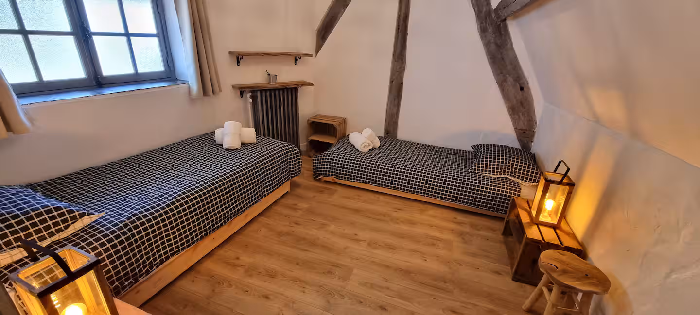 Chambre 4 sous combles avec deux lits simples séparés, parquet bois, charpente apparente et lampes lanterne.