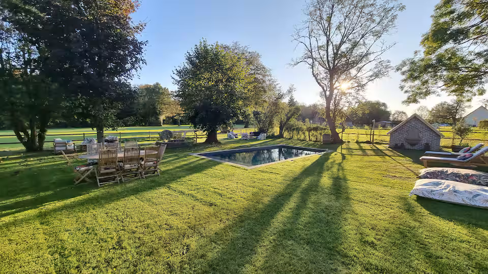 Piscine extérieure entourée de transats, prise en contre-jour au soleil couchant.