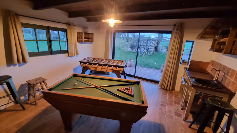 Salle de jeux de la dépendance : billard, baby-foot, kitchenette et grande baie vitrée donnant sur le jardin.