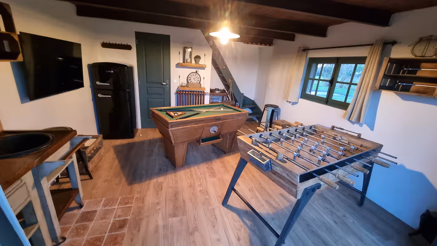 Salle de jeux avec billard, baby-foot, frigo rétro noir et escalier menant à la chambre de la dépendance.