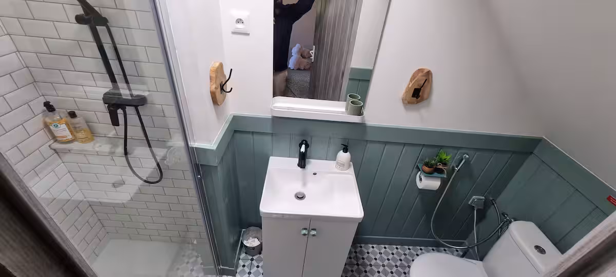 Salle de bain de la dépendance avec lambris vert sauge, douche italienne carreaux métro blancs et lavabo blanc suspendu.