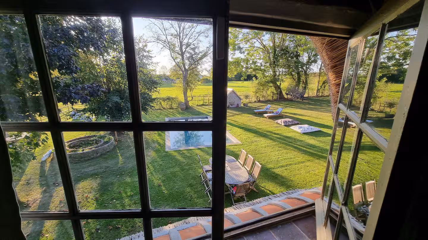 Vue du jardin et de la piscine prise depuis une fenêtre intérieure à petits carreaux.