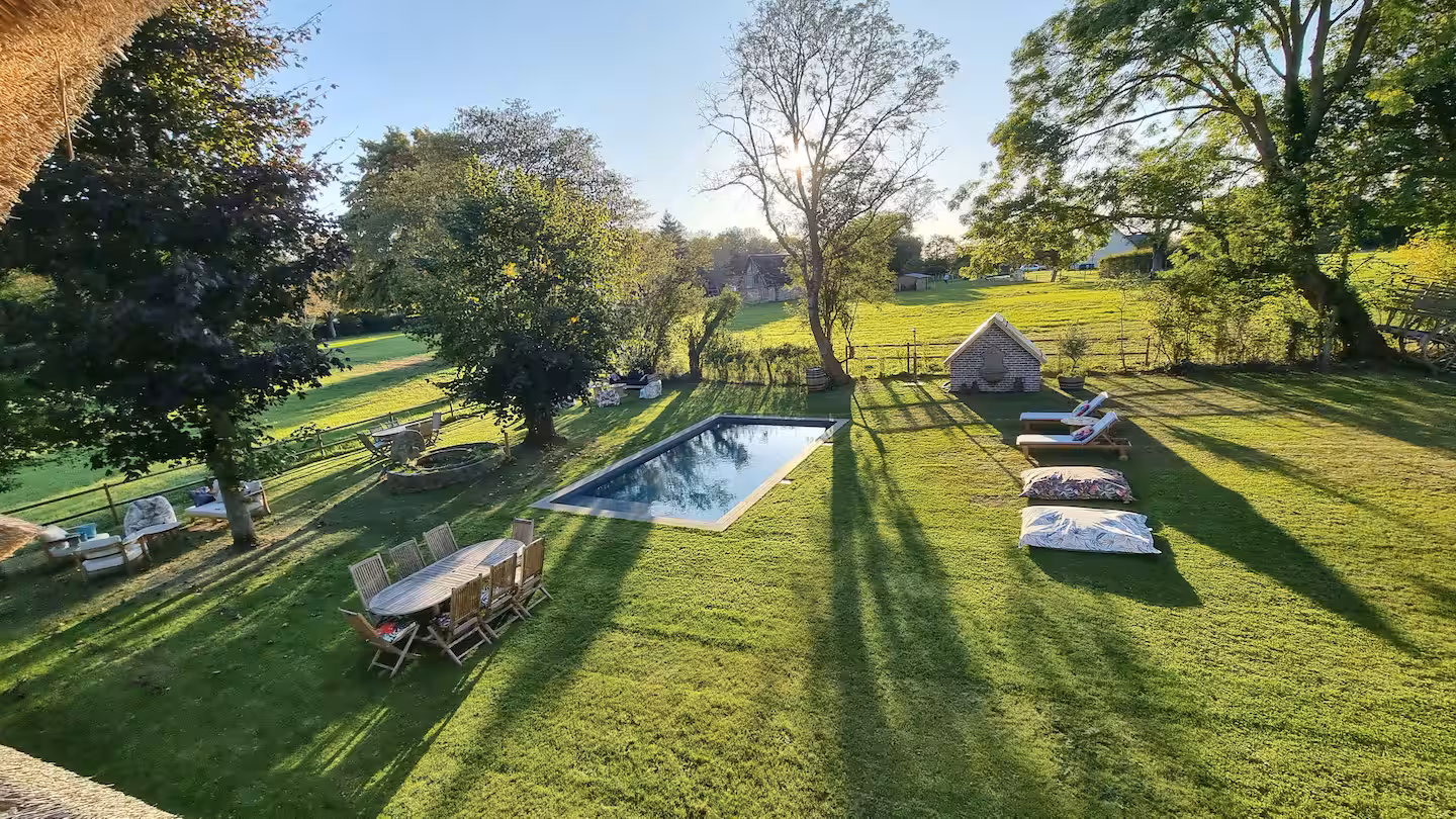 Vue surélevée du parc avec la piscine, la grande table extérieure et les transats.